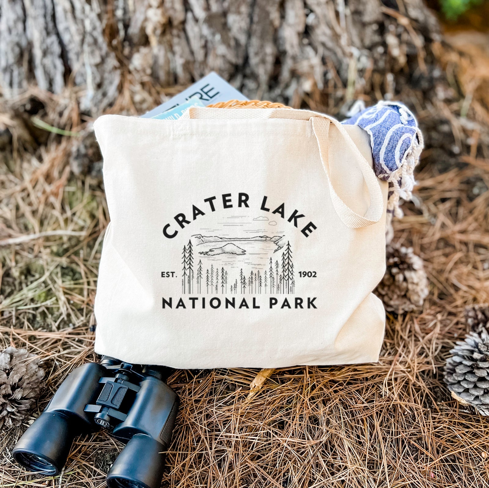 Natural canvas tote bag printed with a round badge of Crater Lake ringed by pine trees, with the words Crater Lake National Park, Est. 1902.