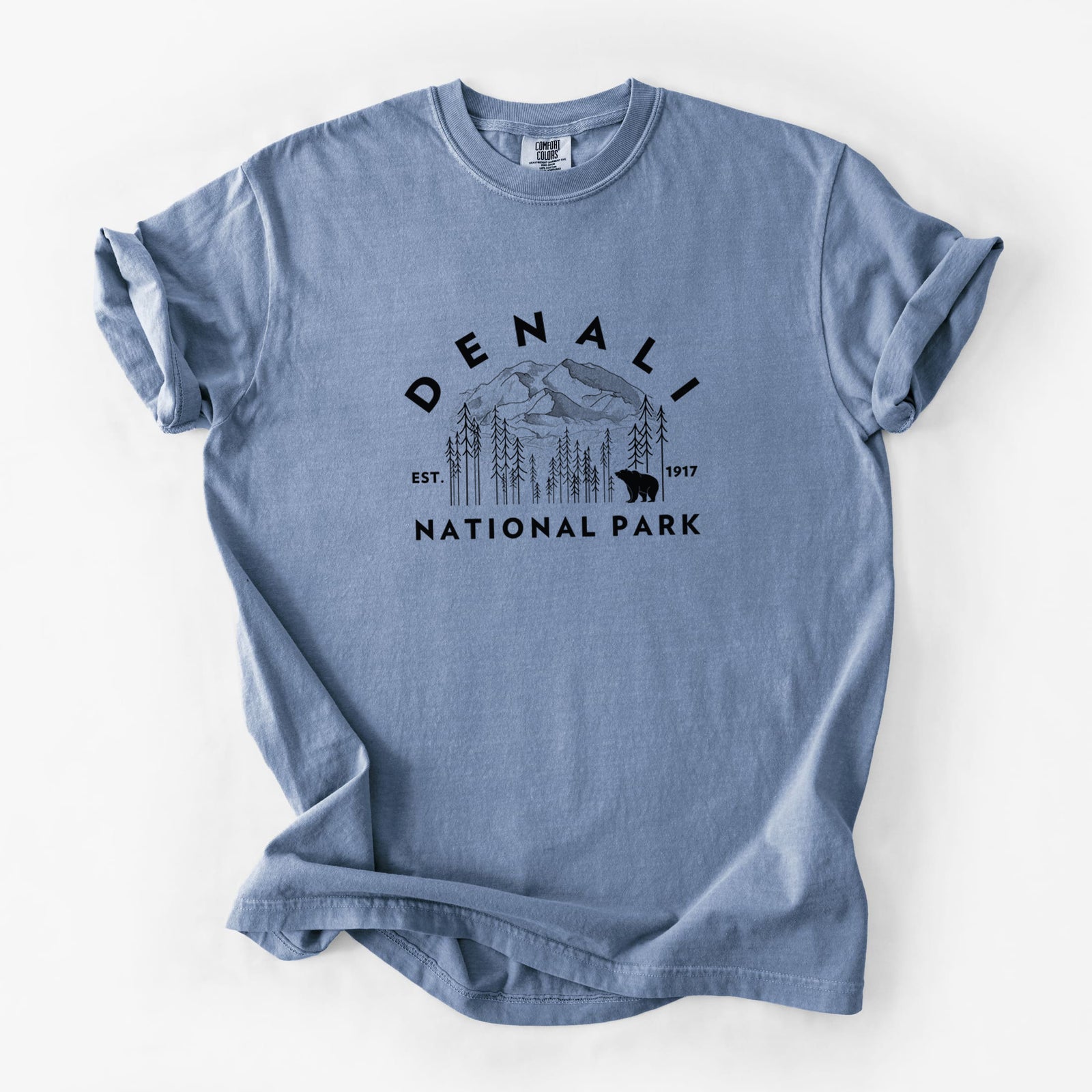 Blue jean Comfort Colors t-shirt laid flat, printed with a round badge of mountains, pine trees and a bear, with the words Denali National Park, Est. 1917.