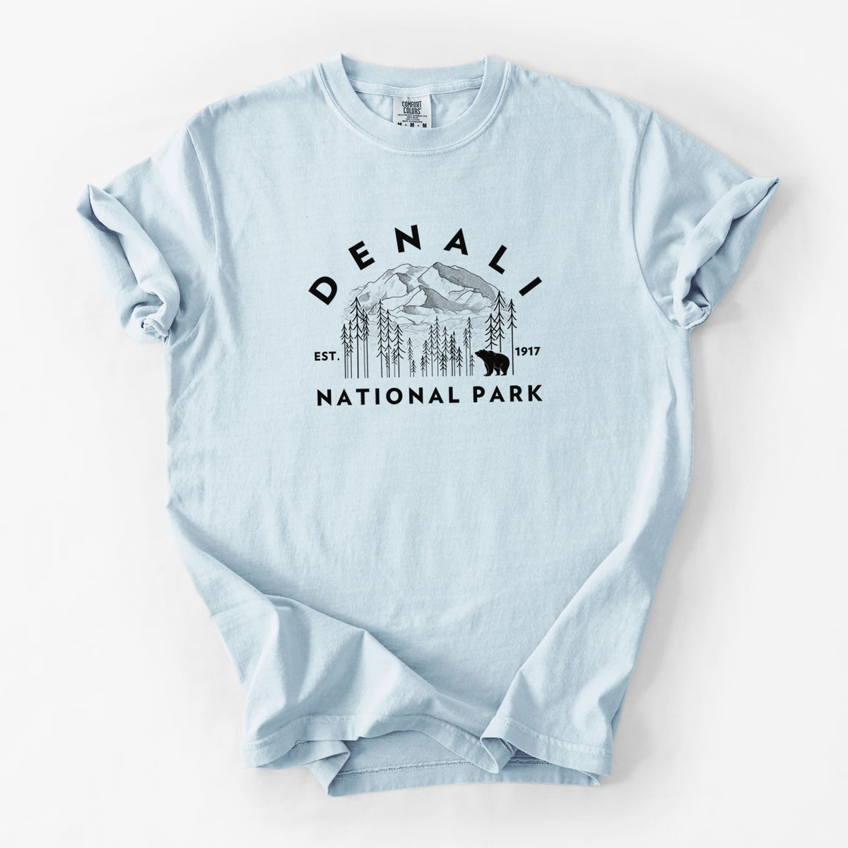 Chambray blue Comfort Colors t-shirt laid flat, printed with a round badge of mountains, pine trees and a bear, with the words Denali National Park, Est. 1917.