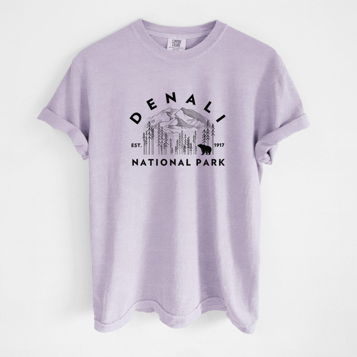 Orchid purple Comfort Colors t-shirt laid flat, printed with a round badge of mountains, pine trees and a bear, with the words Denali National Park, Est. 1917.