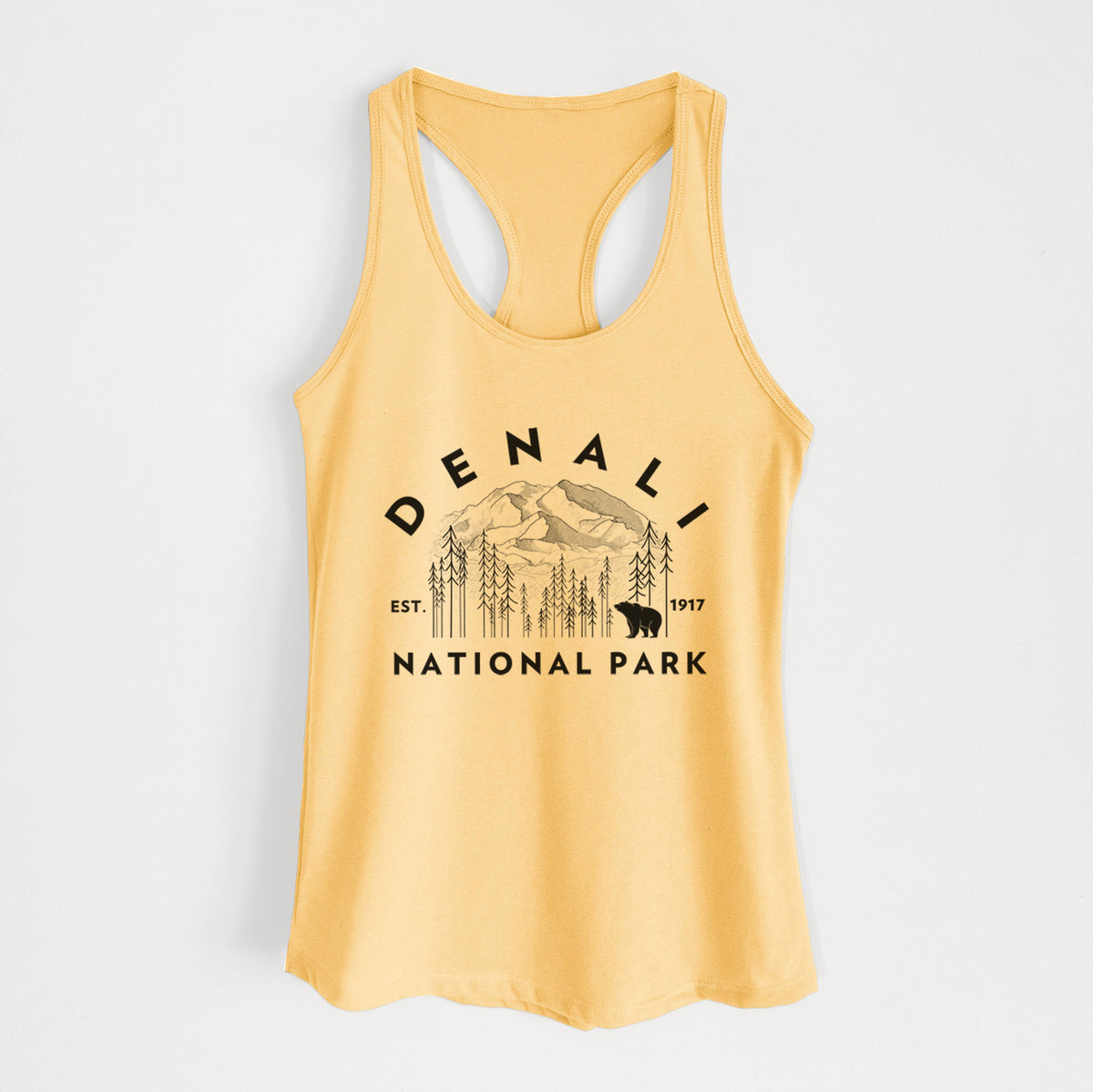 Banana cream women's racerback tank top laid flat, printed with a round badge of mountains, pine trees and a bear, with the words Denali National Park, Est. 1917.