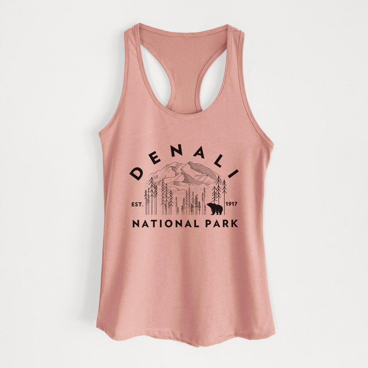 Desert pink women's racerback tank top laid flat, printed with a round badge of mountains, pine trees and a bear, with the words Denali National Park, Est. 1917.