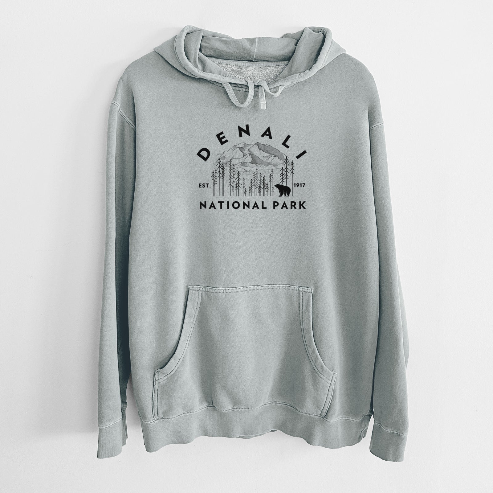 Sage green pigment dyed hoodie laid flat, printed with a round badge of mountains, pine trees and a bear, with the words Denali National Park, Est. 1917.