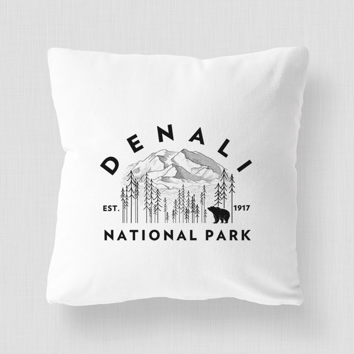 White pillow cover printed with a round badge of mountains, pine trees and a bear, with the words Denali National Park, Est. 1917.