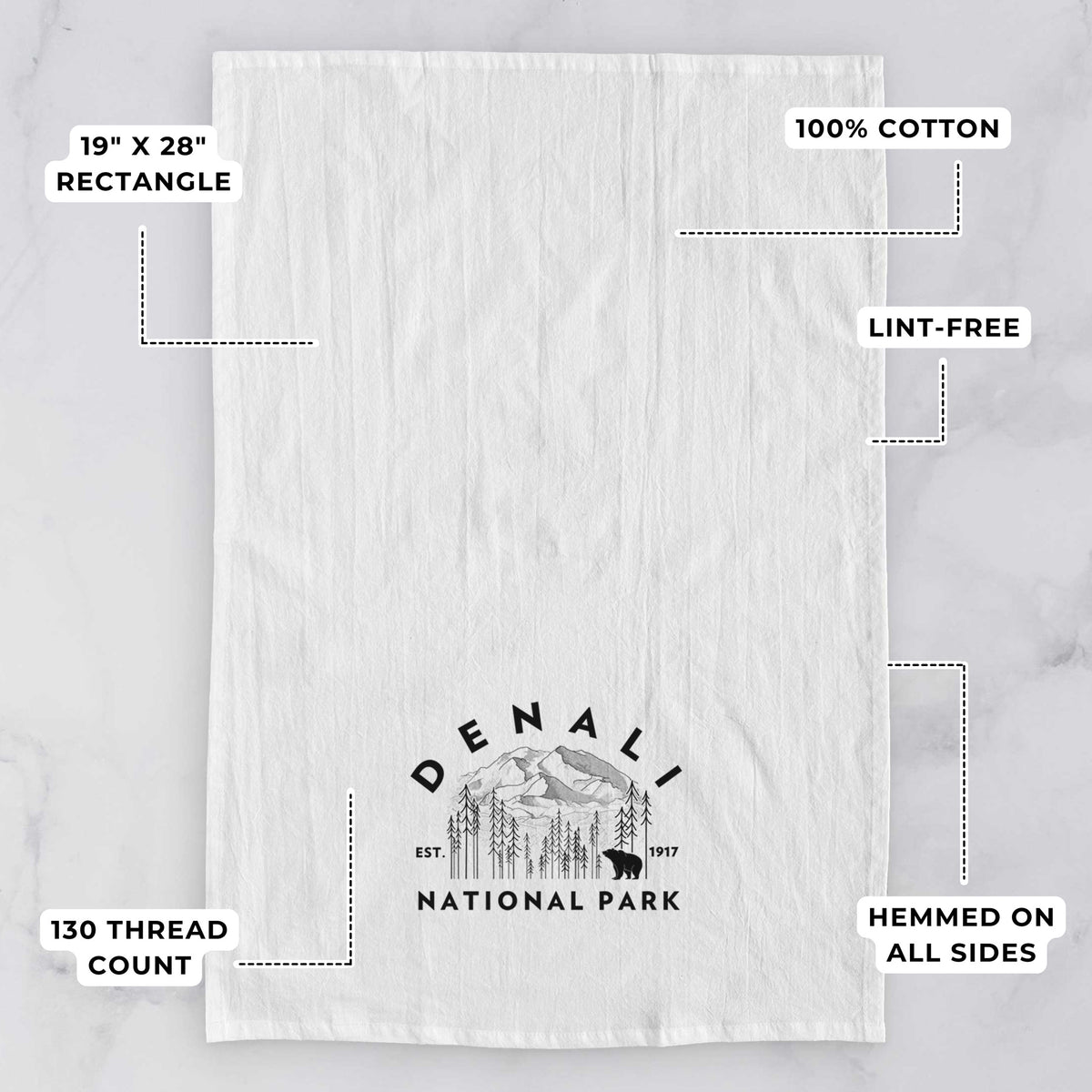 White tea towel printed with a round badge of mountains, pine trees and a bear, with the words Denali National Park, Est. 1917, with feature labels: 19 by 28 inch rectangle, 100% cotton, lint-free, 130 thread count, hemmed on all sides.