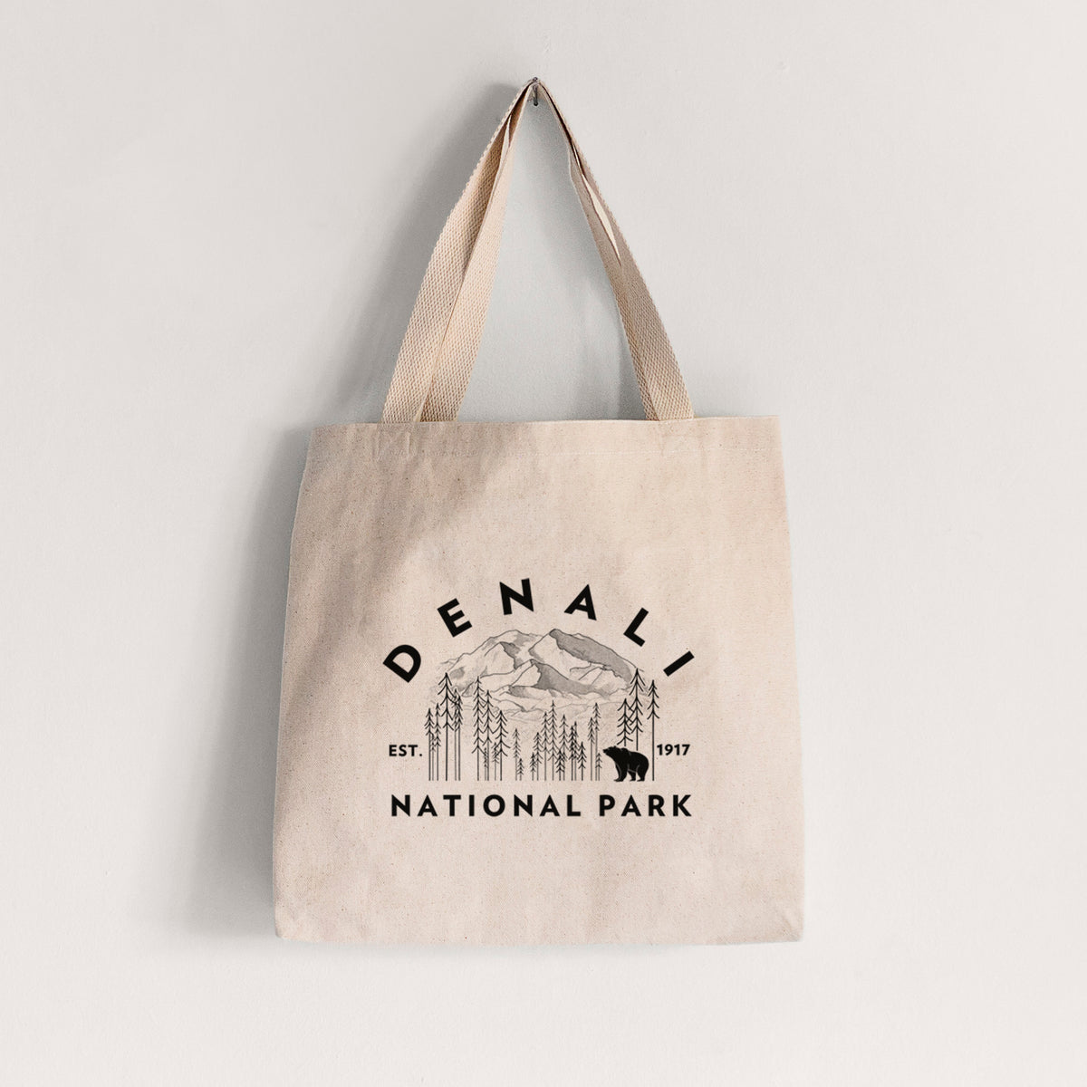 Natural canvas tote bag printed with a round badge of mountains, pine trees and a bear, with the words Denali National Park, Est. 1917.