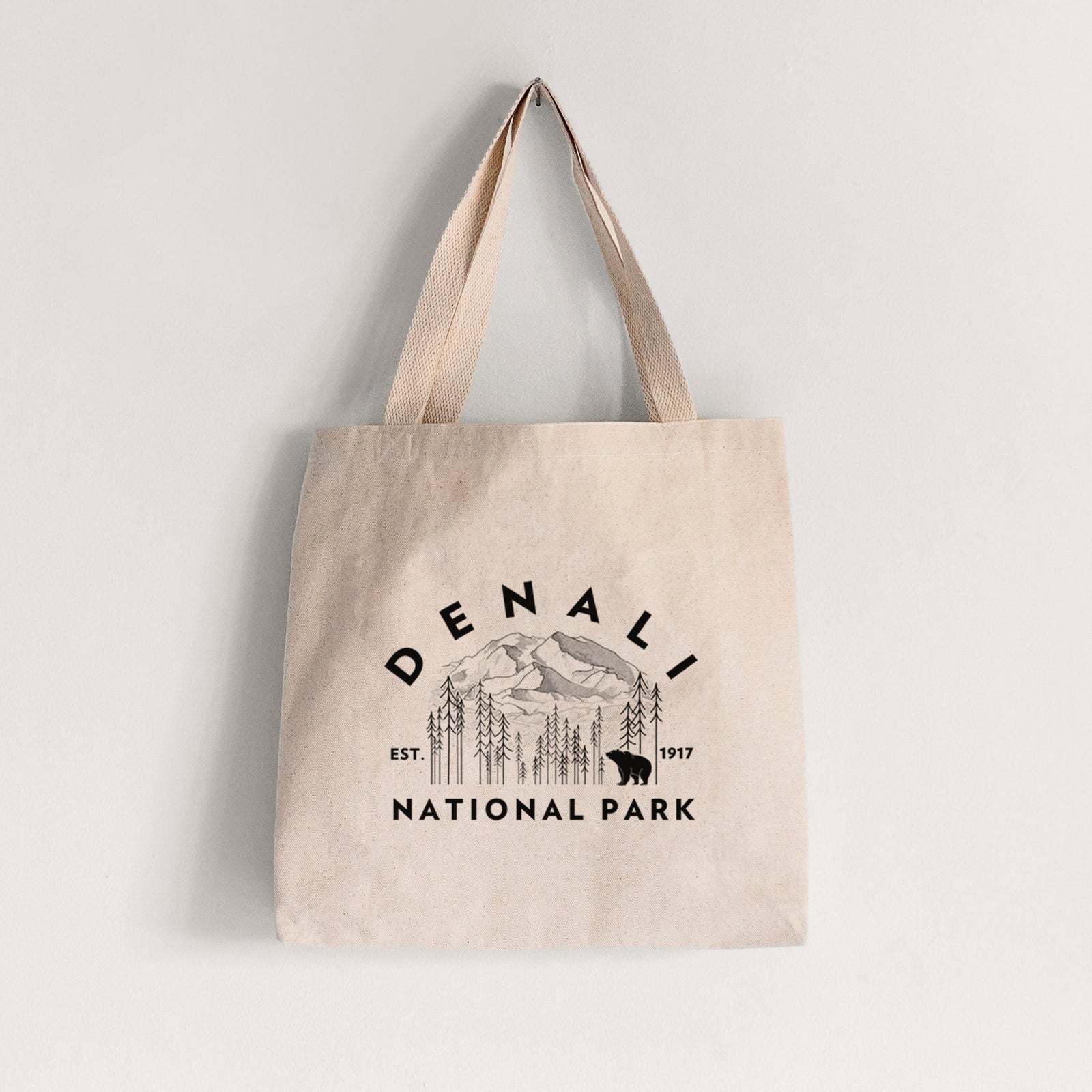 Natural canvas tote bag printed with a round badge of mountains, pine trees and a bear, with the words Denali National Park, Est. 1917.