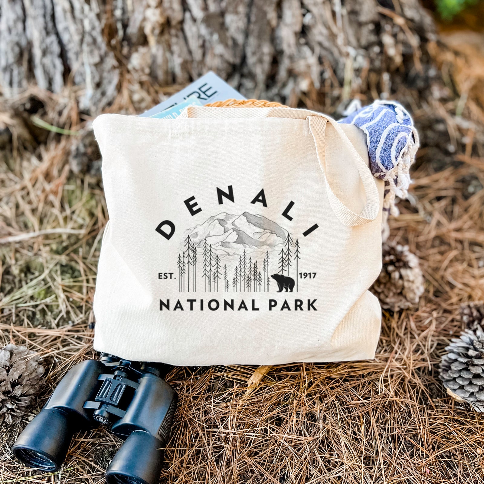 Natural canvas tote bag printed with a round badge of mountains, pine trees and a bear, with the words Denali National Park, Est. 1917.
