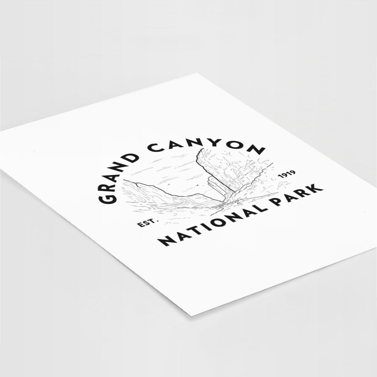 Art print of a round badge of canyon cliffs, with the words Grand Canyon National Park, Est. 1919, lying at an angle on a white surface.