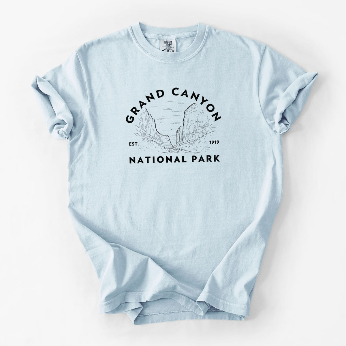 Chambray blue Comfort Colors t-shirt laid flat, printed with a round badge of canyon cliffs, with the words Grand Canyon National Park, Est. 1919.
