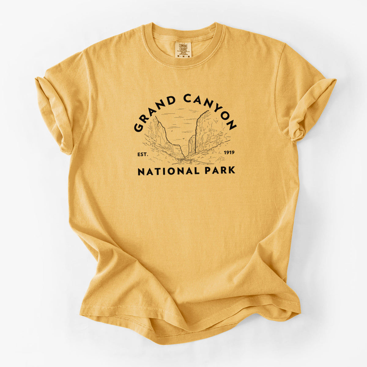 Golden wheat yellow Comfort Colors t-shirt laid flat, printed with a round badge of canyon cliffs, with the words Grand Canyon National Park, Est. 1919.