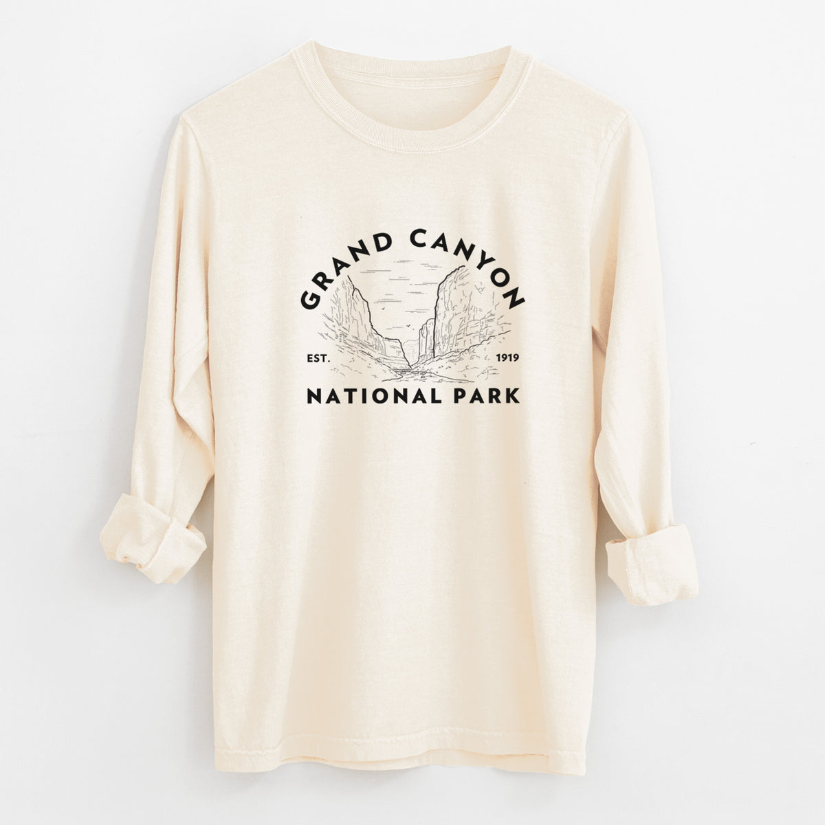 Ivory Comfort Colors long sleeve shirt laid flat with the cuffs rolled, printed with a round badge of canyon cliffs, with the words Grand Canyon National Park, Est. 1919.