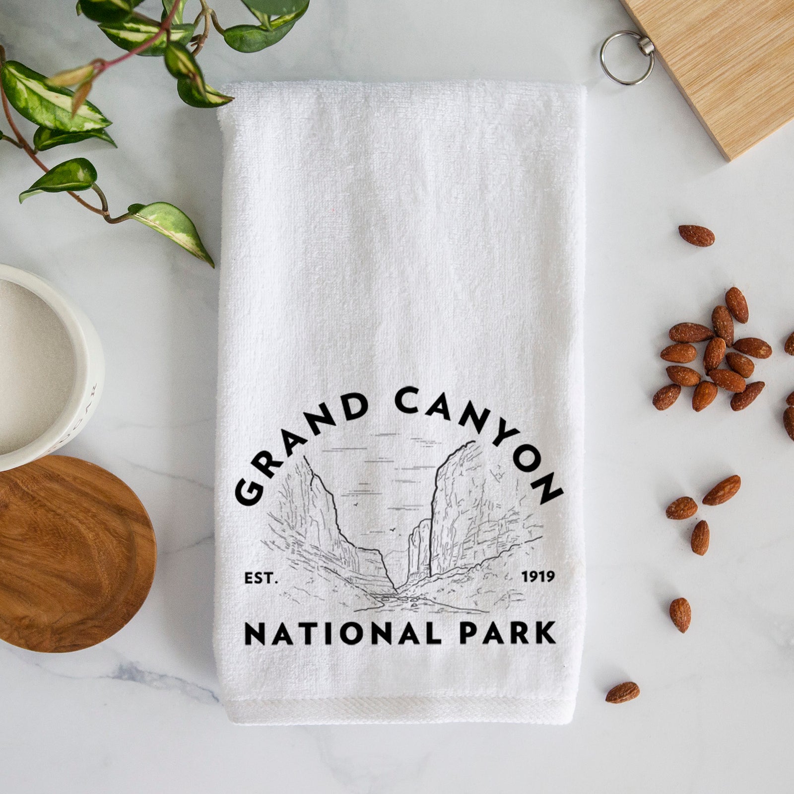 White hand towel printed with a round badge of canyon cliffs, with the words Grand Canyon National Park, Est. 1919.