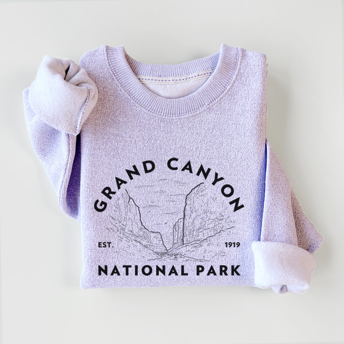 Ice purple knit sweatshirt printed with a round badge of canyon cliffs, with the words Grand Canyon National Park, Est. 1919, styled flat.