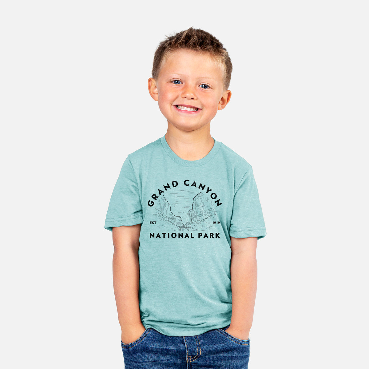 Smiling boy wearing a youth t-shirt printed with a round badge of canyon cliffs, with the words Grand Canyon National Park, Est. 1919.
