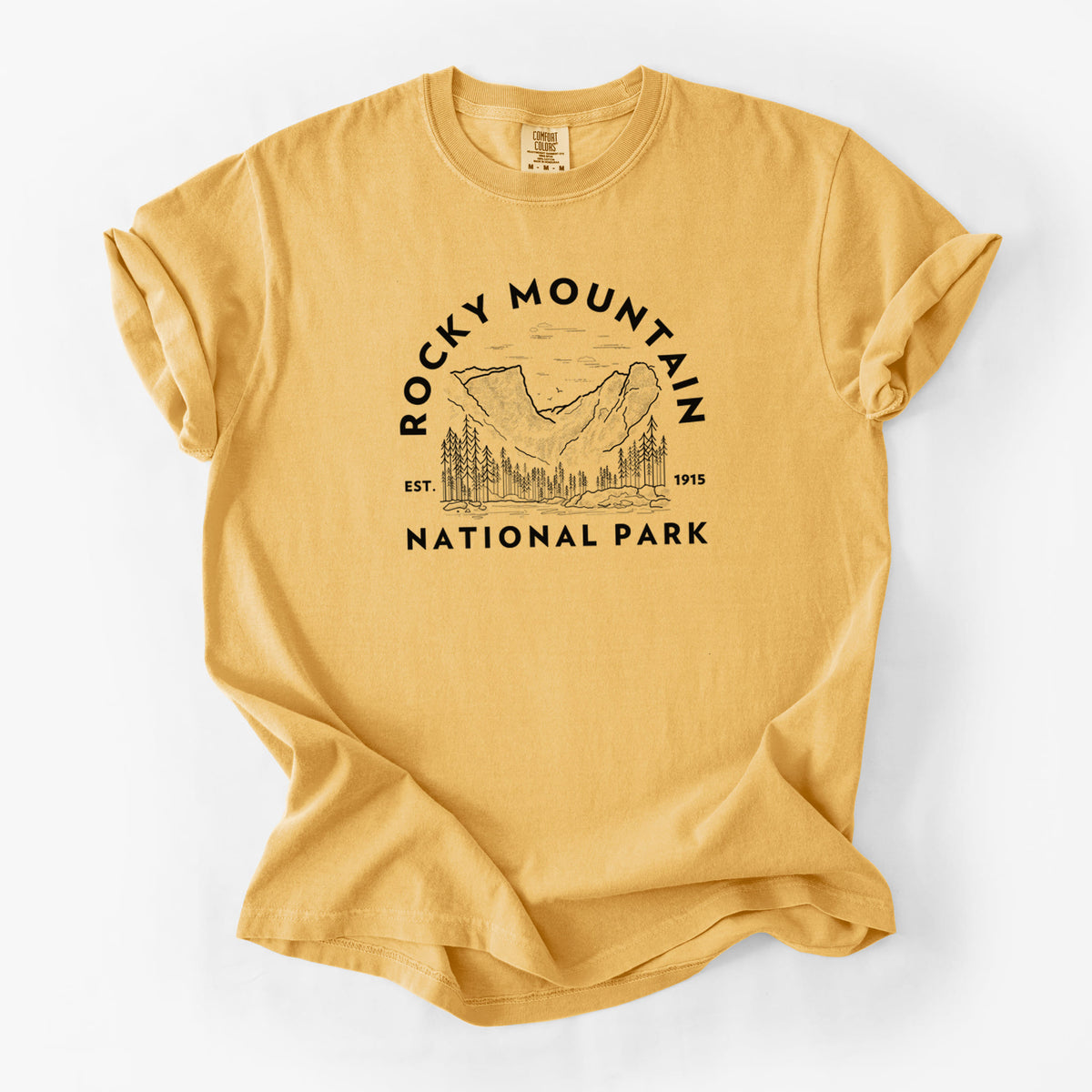 Golden wheat yellow Comfort Colors t-shirt laid flat, printed with a round badge of mountains and pine trees, with the words Rocky Mountain National Park, Est. 1915.