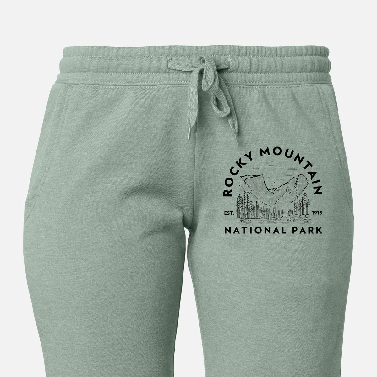 Front of sage green Cali Wave sweatpants, printed with a round badge of mountains and pine trees, with the words Rocky Mountain National Park, Est. 1915 on the leg.