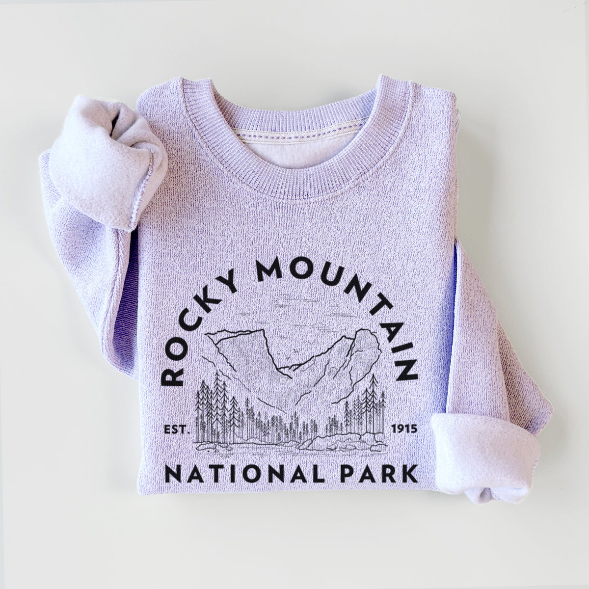 Ice purple knit sweatshirt printed with a round badge of mountains and pine trees, with the words Rocky Mountain National Park, Est. 1915, styled flat.
