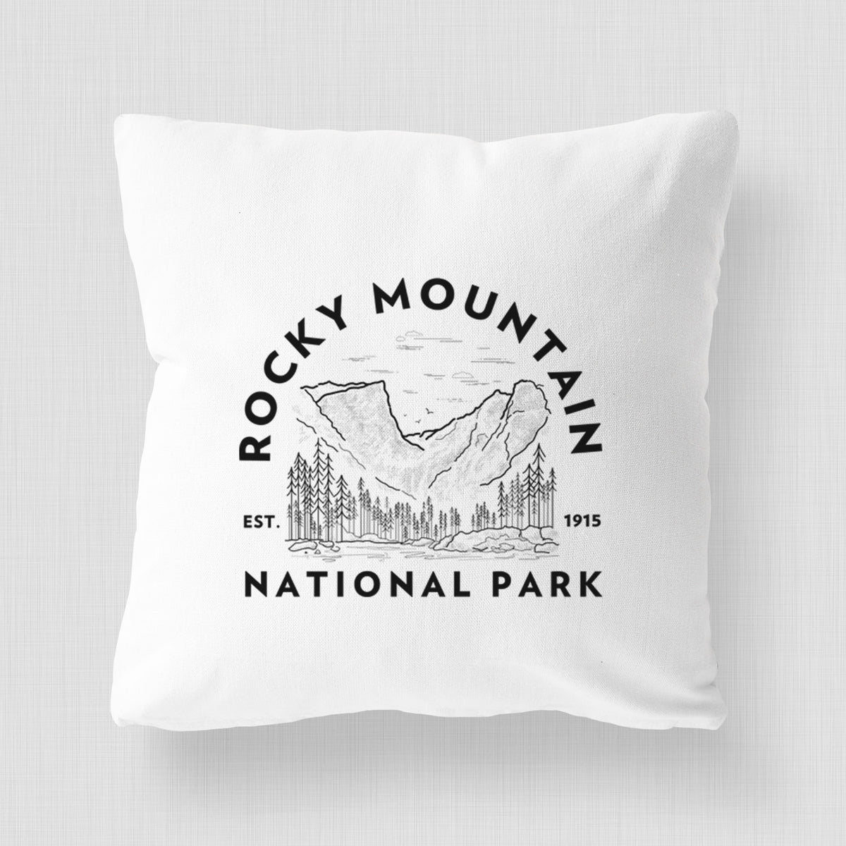 White pillow cover printed with a round badge of mountains and pine trees, with the words Rocky Mountain National Park, Est. 1915.
