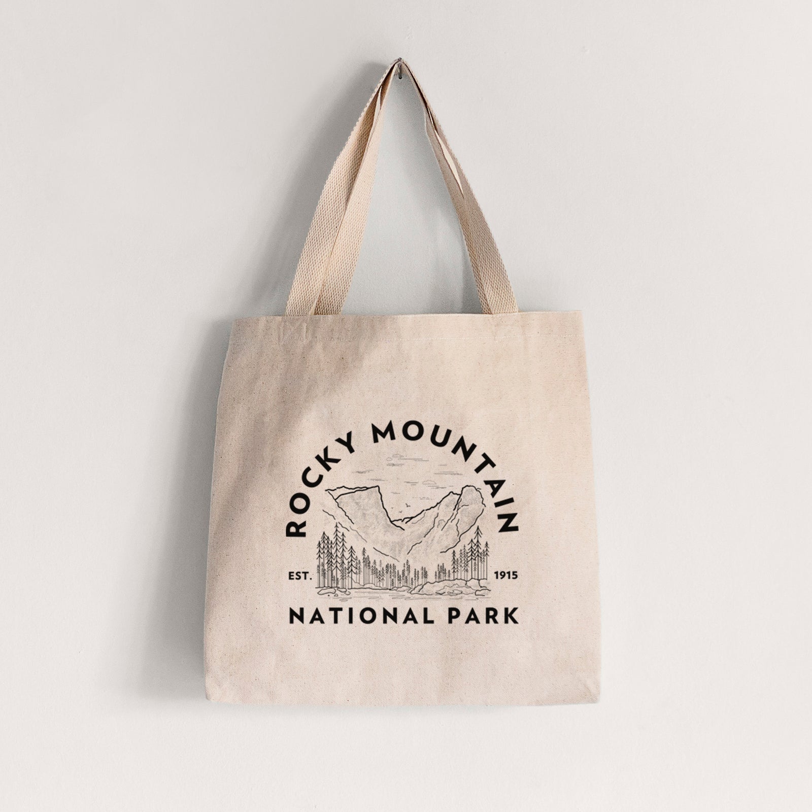 Natural canvas tote bag printed with a round badge of mountains and pine trees, with the words Rocky Mountain National Park, Est. 1915.