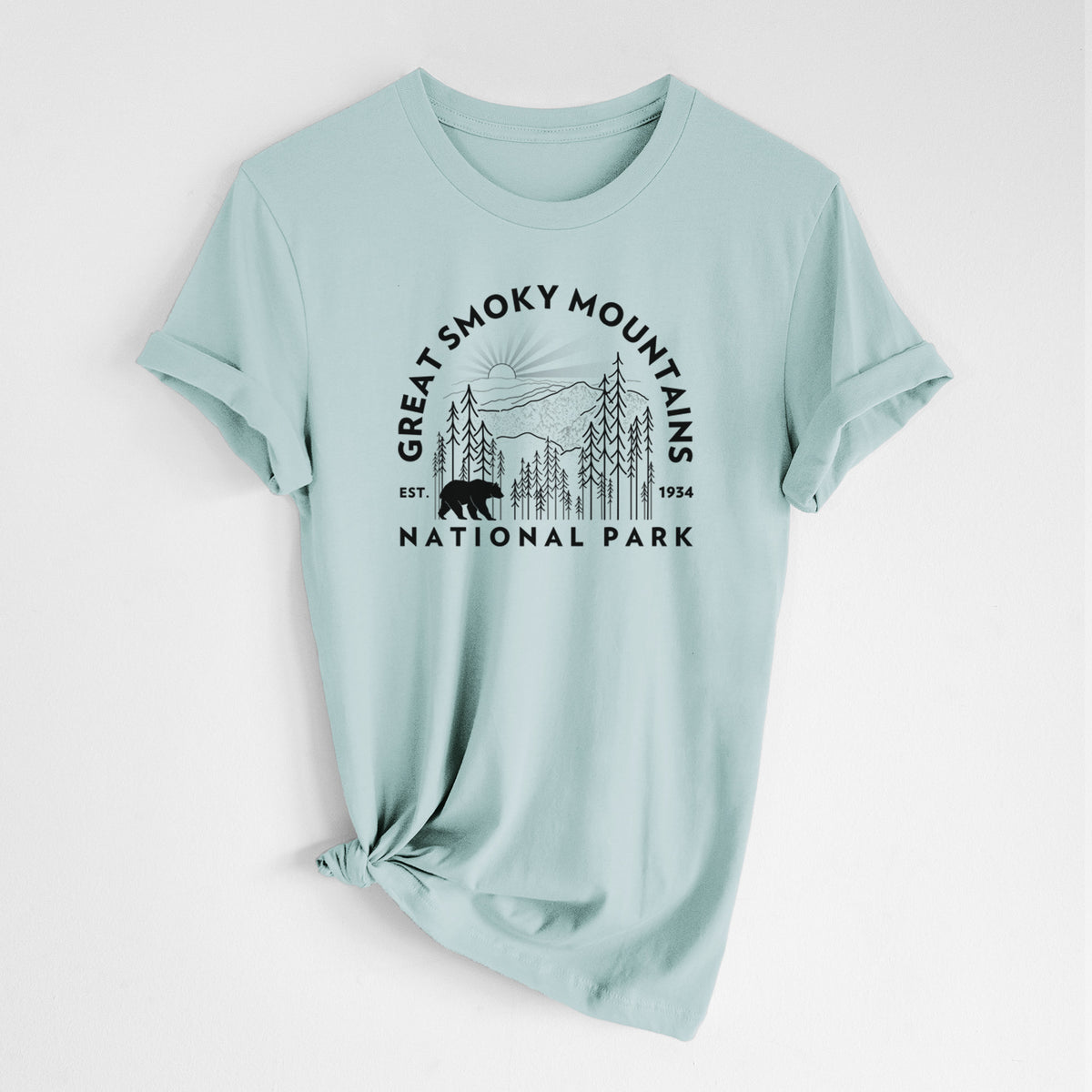 Dusty blue lightweight cotton t-shirt laid flat with the sleeves rolled, printed with a round badge of mountains, pine trees and a black bear, with the words Great Smoky Mountains National Park, Est. 1934.