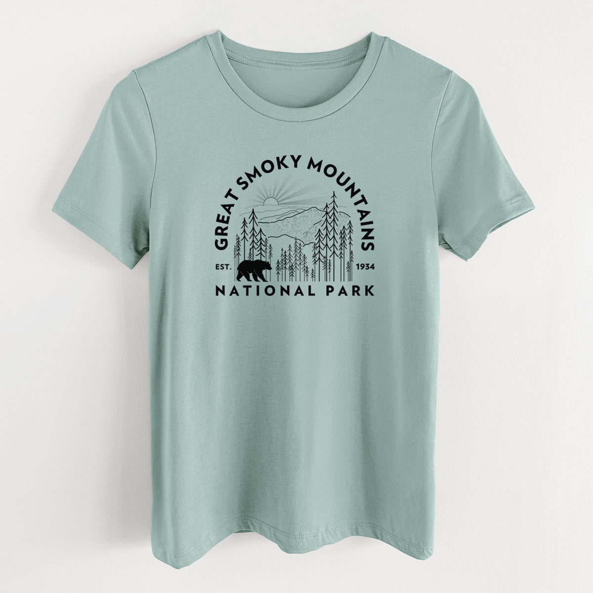 Dusty blue women's relaxed fit cotton t-shirt laid flat, printed with a round badge of mountains, pine trees and a black bear, with the words Great Smoky Mountains National Park, Est. 1934.