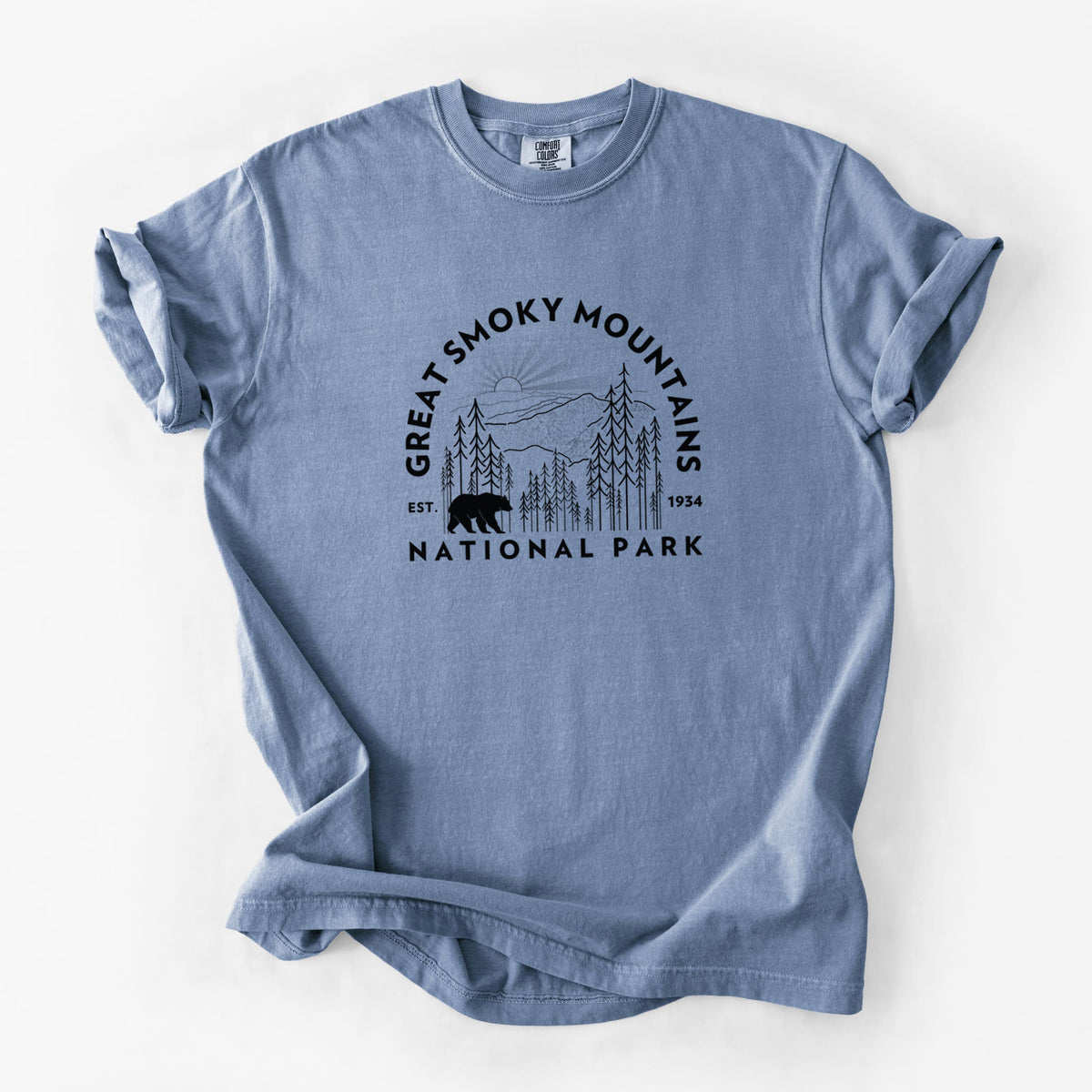 Blue jean Comfort Colors t-shirt laid flat, printed with a round badge of mountains, pine trees and a black bear, with the words Great Smoky Mountains National Park, Est. 1934.
