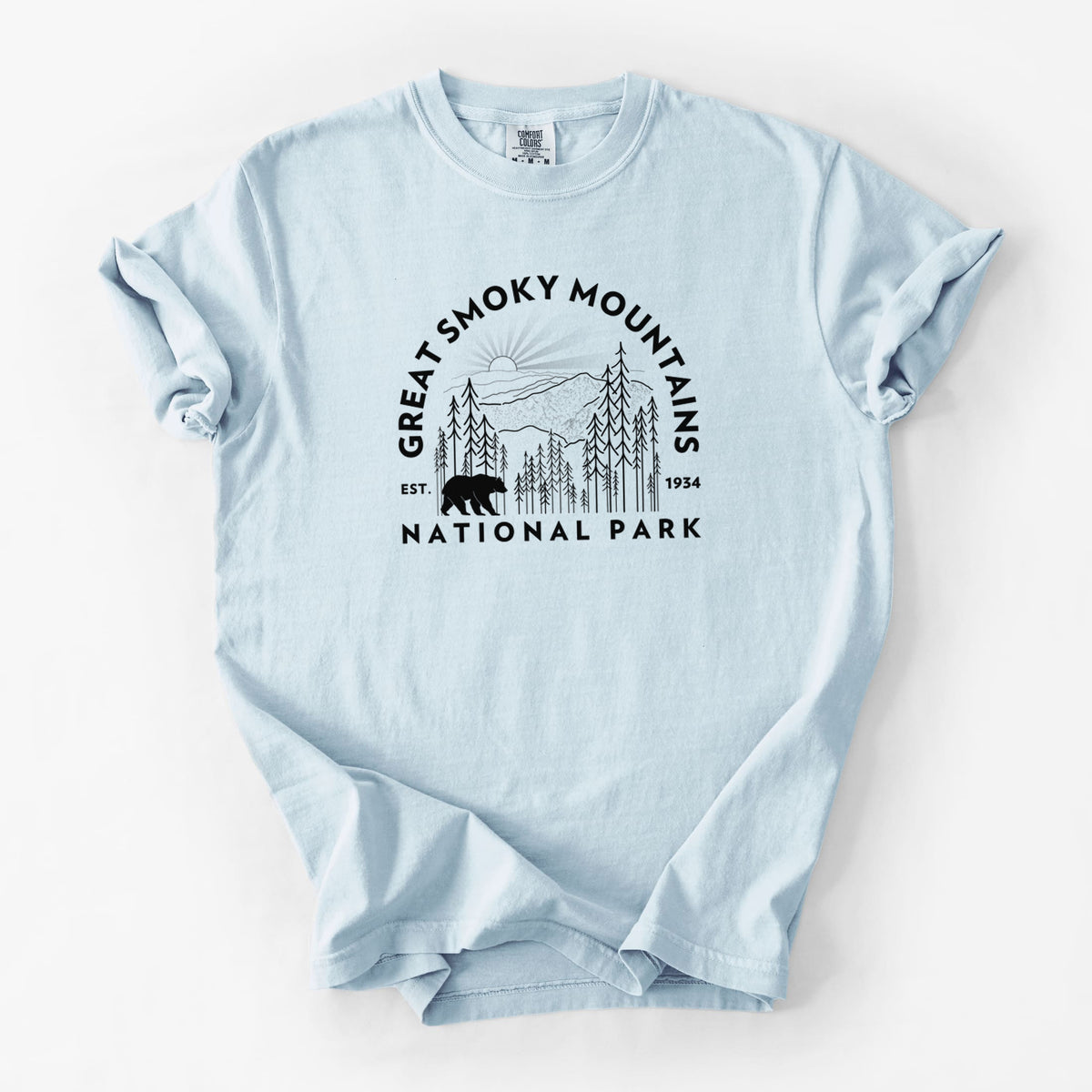 Chambray blue Comfort Colors t-shirt laid flat, printed with a round badge of mountains, pine trees and a black bear, with the words Great Smoky Mountains National Park, Est. 1934.
