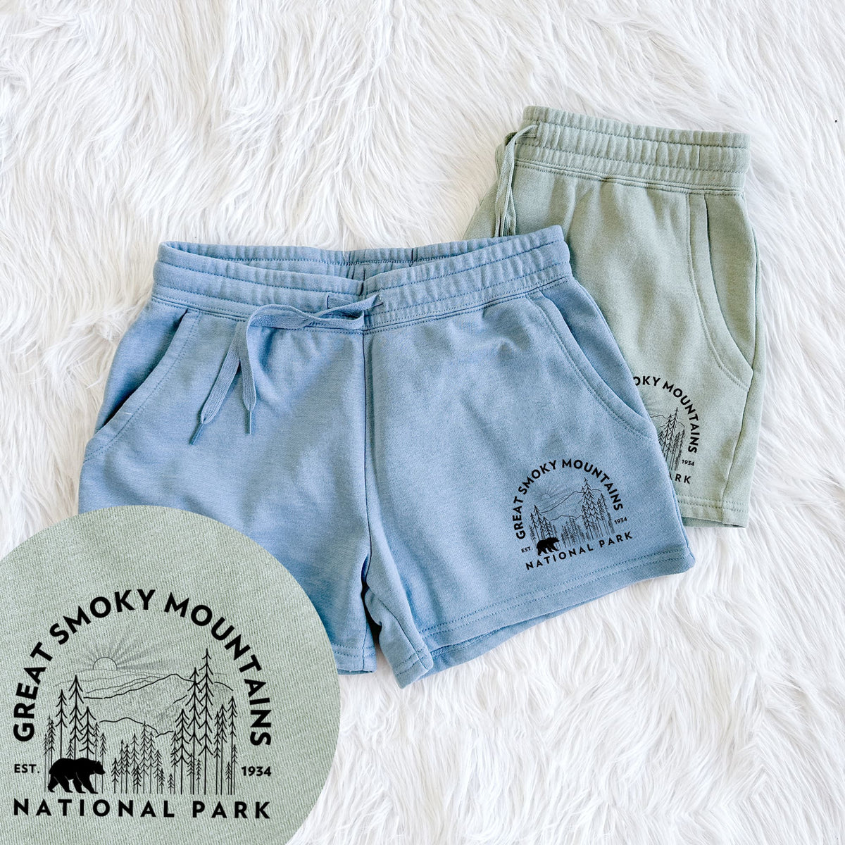 Two pairs of Cali Wave shorts in different colors printed with a round badge of mountains, pine trees and a black bear, with the words Great Smoky Mountains National Park, Est. 1934, with a close-up of the print.