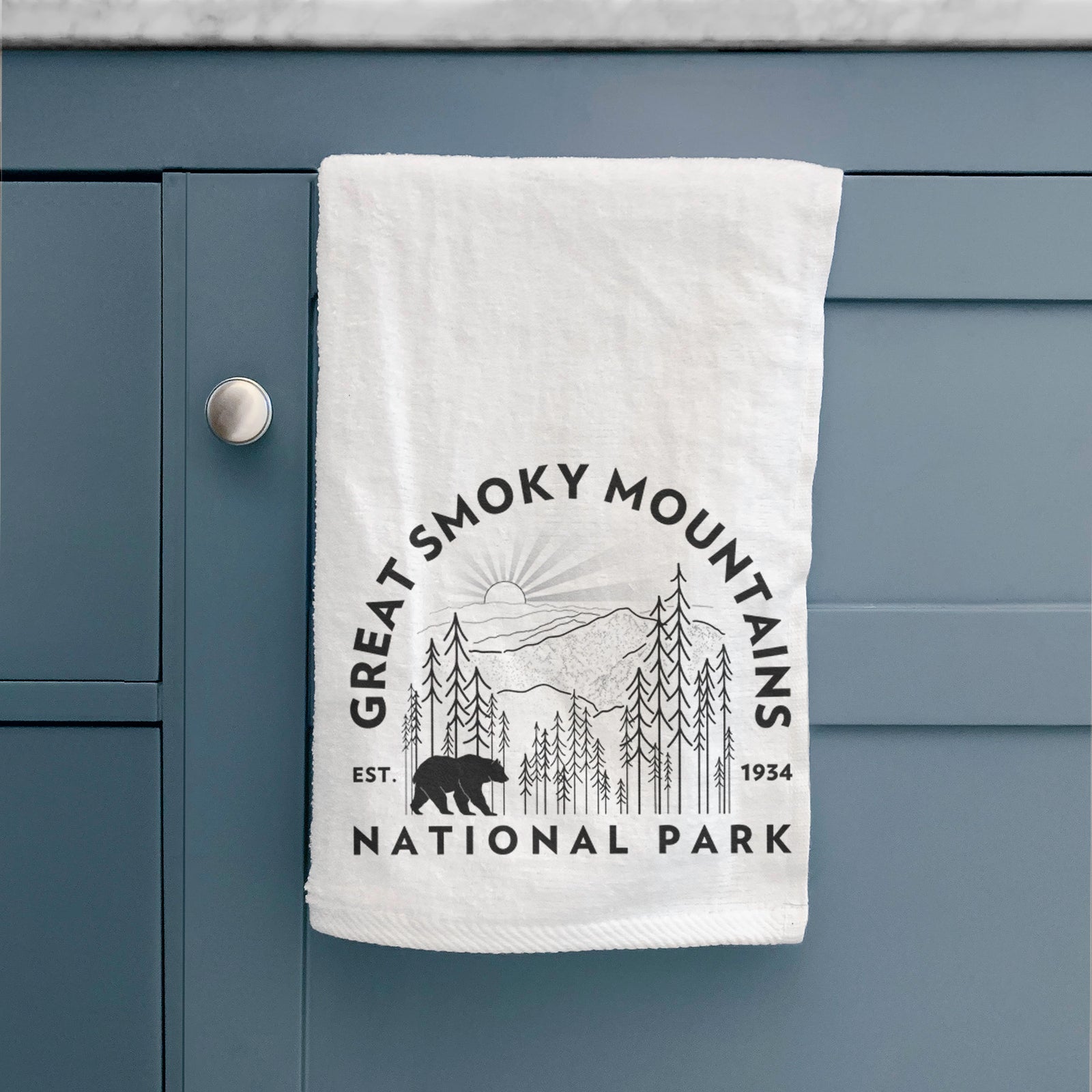 White hand towel printed with a round badge of mountains, pine trees and a black bear, with the words Great Smoky Mountains National Park, Est. 1934.