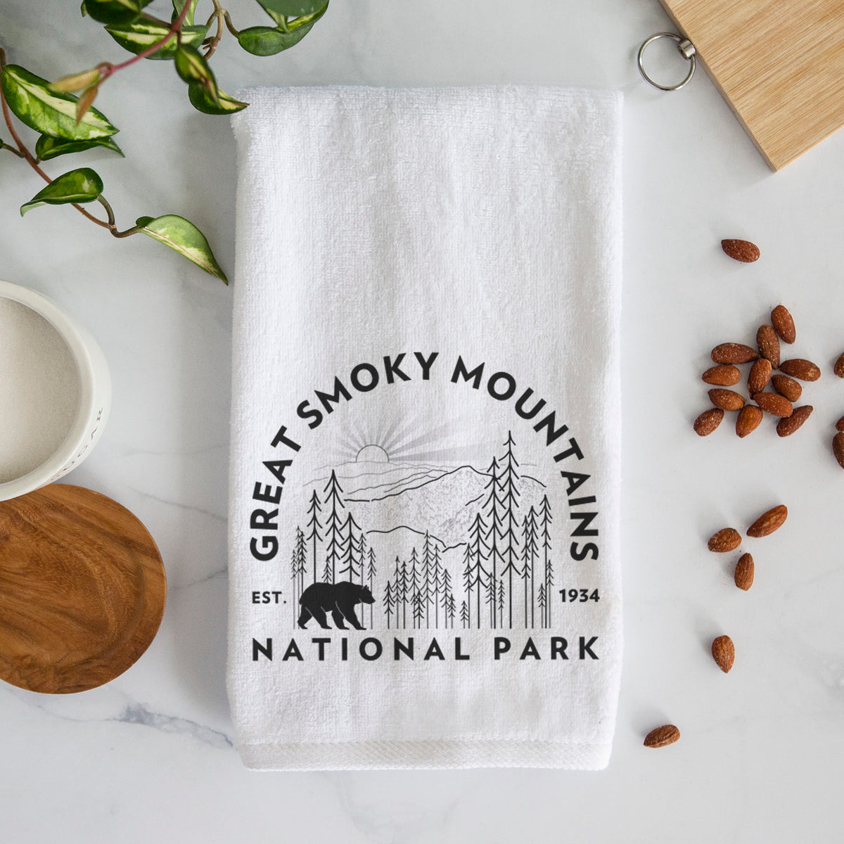 White hand towel printed with a round badge of mountains, pine trees and a black bear, with the words Great Smoky Mountains National Park, Est. 1934.
