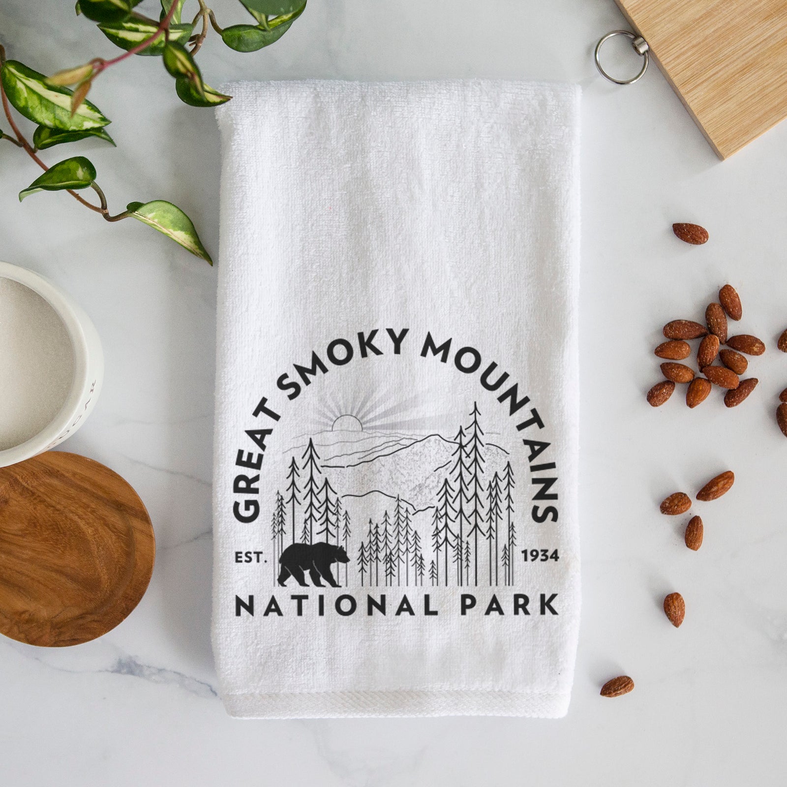 White hand towel printed with a round badge of mountains, pine trees and a black bear, with the words Great Smoky Mountains National Park, Est. 1934.