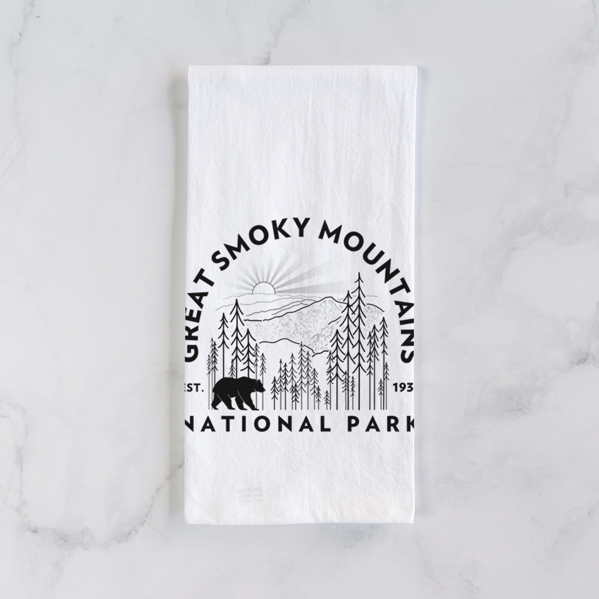 White cotton tea towel laid flat on marble, printed with a round badge of mountains, pine trees and a black bear, with the words Great Smoky Mountains National Park, Est. 1934.