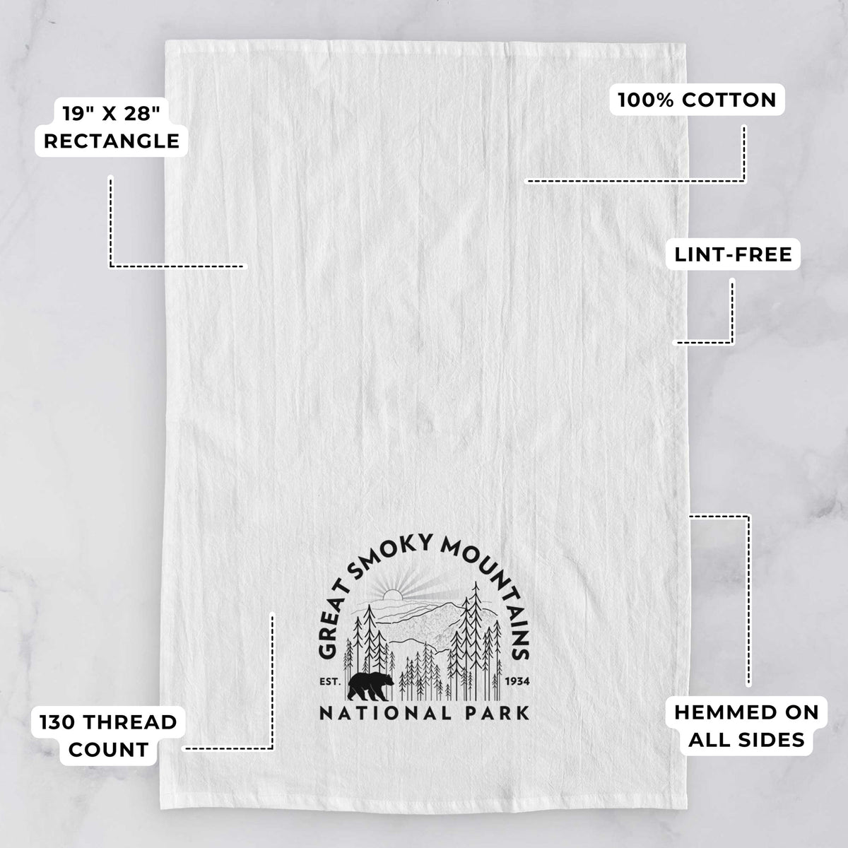 White tea towel printed with a round badge of mountains, pine trees and a black bear, with the words Great Smoky Mountains National Park, Est. 1934, with feature labels: 19 by 28 inch rectangle, 100% cotton, lint-free, 130 thread count, hemmed on all sides.