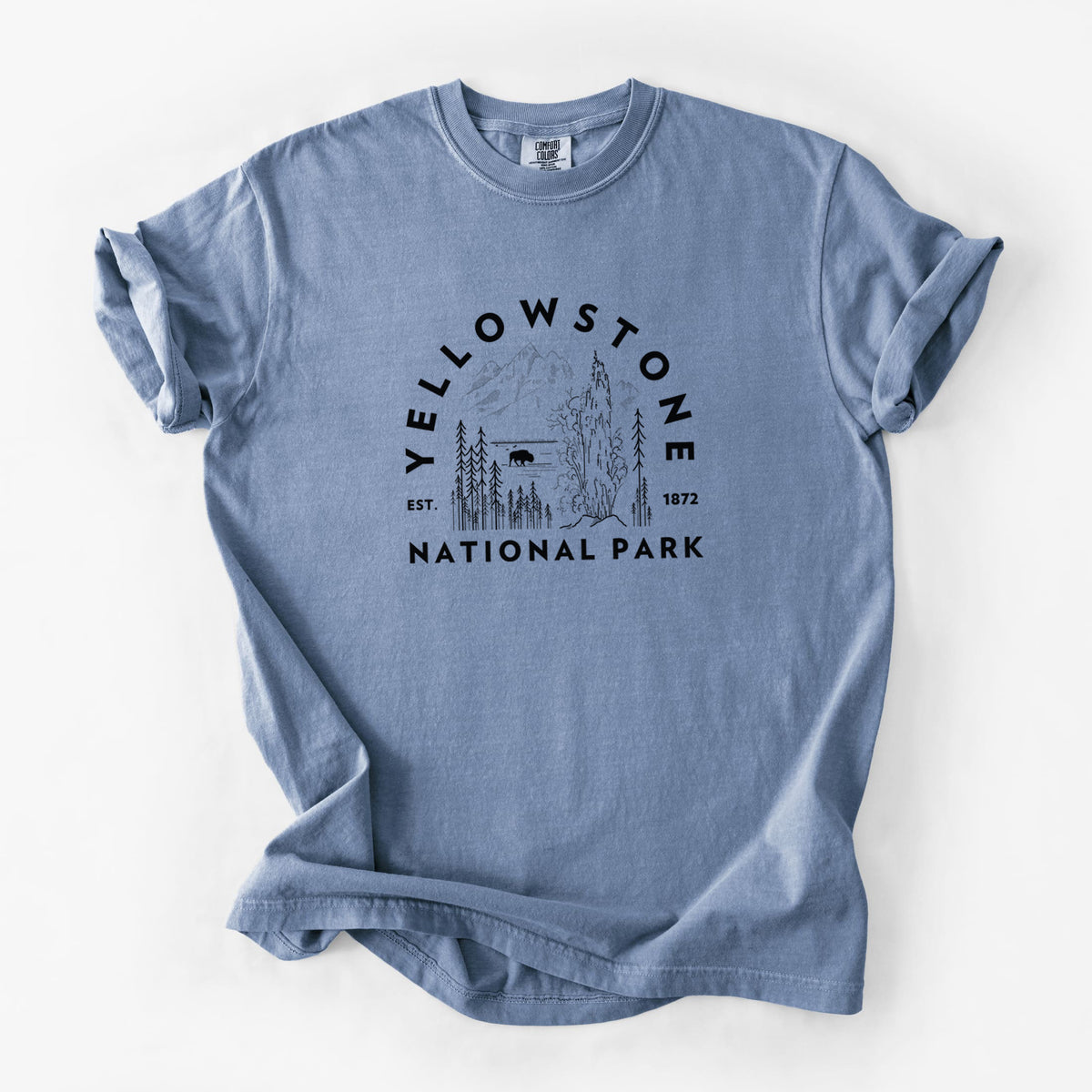 Blue jean Comfort Colors t-shirt laid flat, printed with a round badge of a waterfall, pine trees and a bison, with the words Yellowstone National Park, Est. 1872.