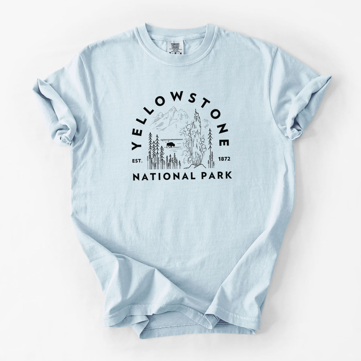 Chambray blue Comfort Colors t-shirt laid flat, printed with a round badge of a waterfall, pine trees and a bison, with the words Yellowstone National Park, Est. 1872.