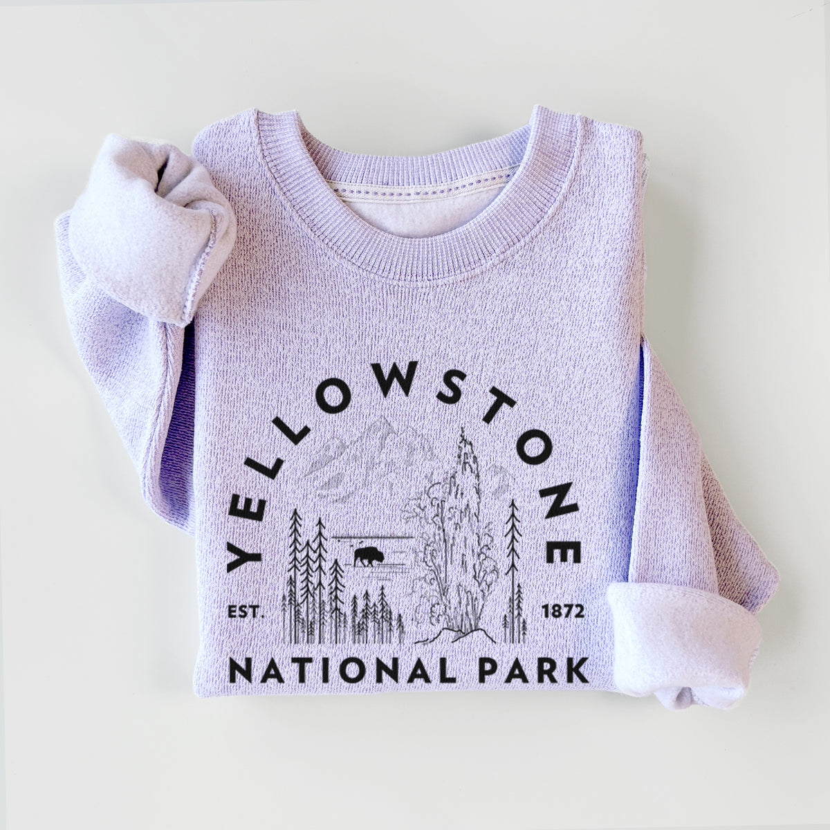 Ice purple knit sweatshirt printed with a round badge of a waterfall, pine trees and a bison, with the words Yellowstone National Park, Est. 1872, styled flat.