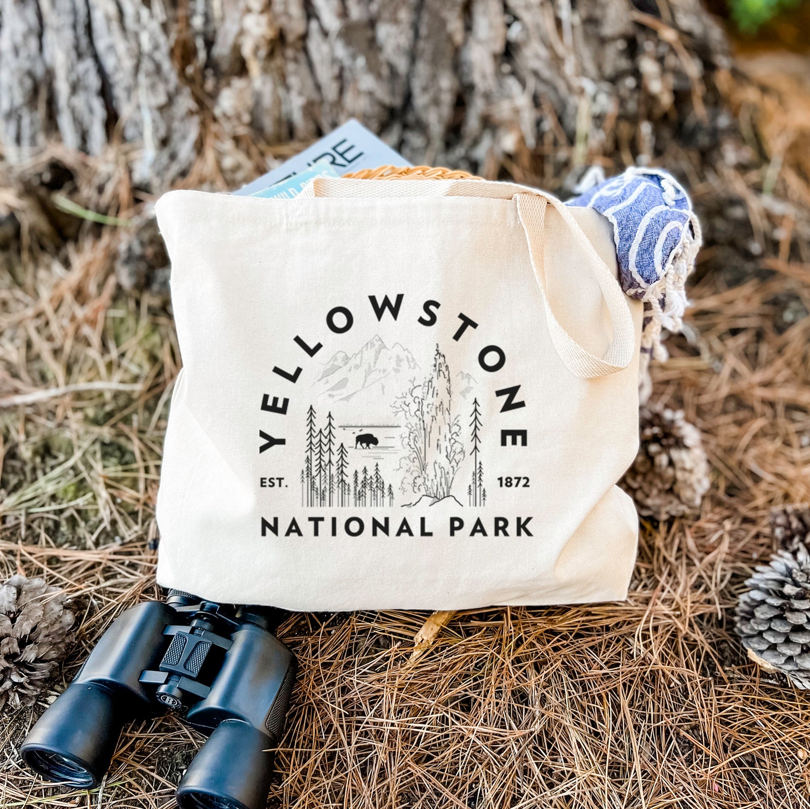 Natural canvas tote bag printed with a round badge of a waterfall, pine trees and a bison, with the words Yellowstone National Park, Est. 1872.