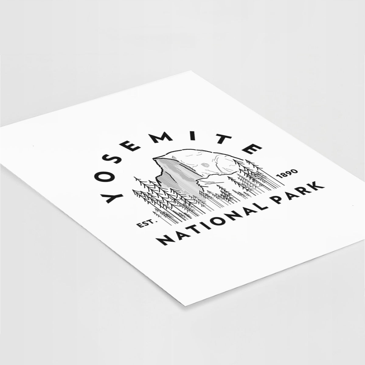 Art print of a round badge of Half Dome and pine trees, with the words Yosemite National Park, Est. 1890, lying at an angle on a white surface.