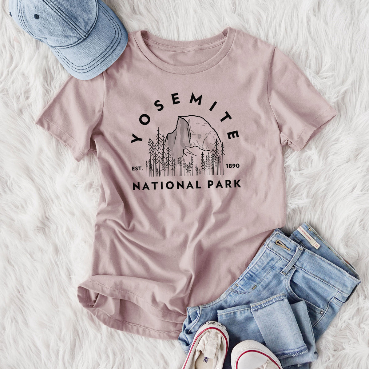 Women's relaxed fit cotton t-shirt printed with a round badge of Half Dome and pine trees, with the words Yosemite National Park, Est. 1890, styled flat on a white faux fur rug with jeans.