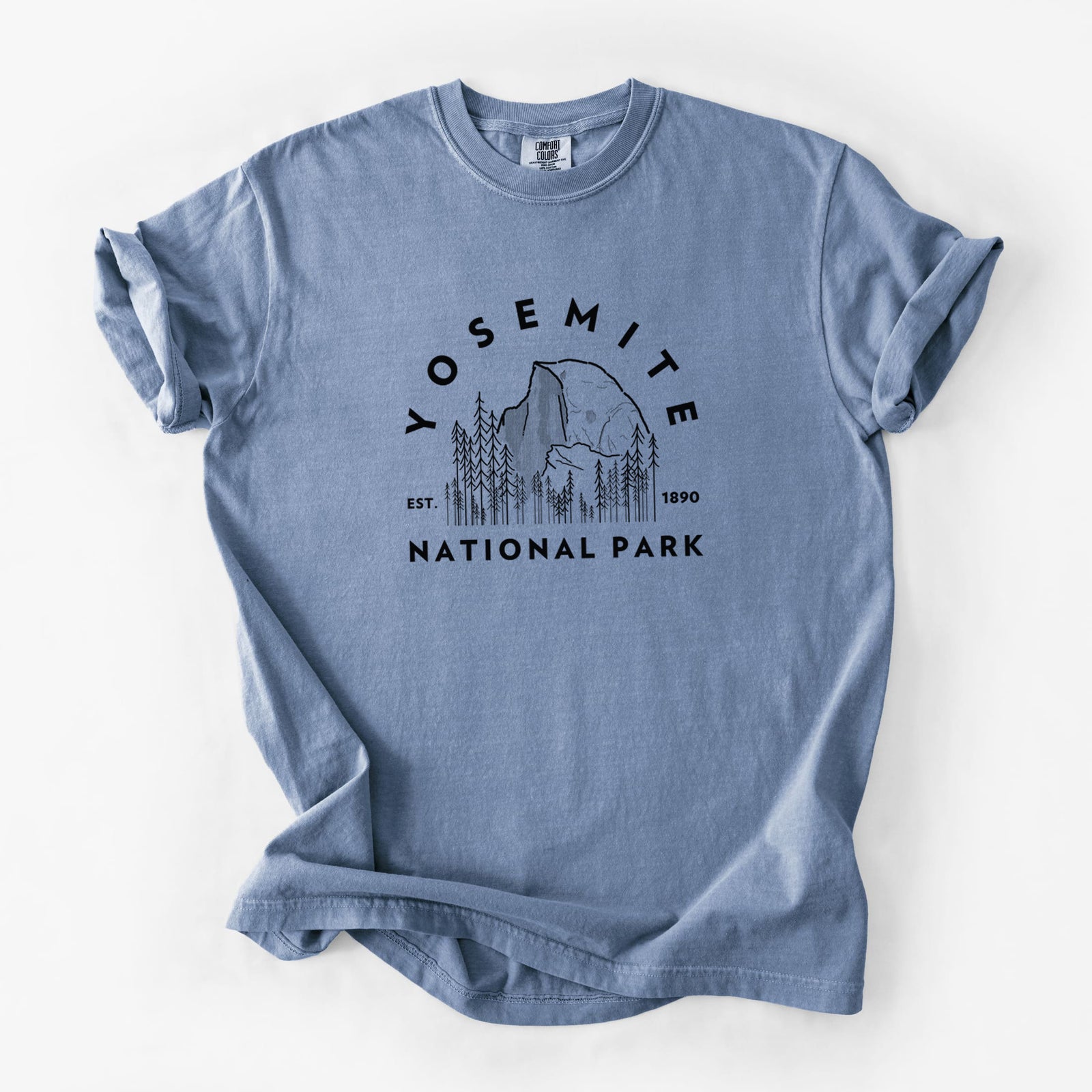 Blue jean Comfort Colors t-shirt laid flat, printed with a round badge of Half Dome and pine trees, with the words Yosemite National Park, Est. 1890.