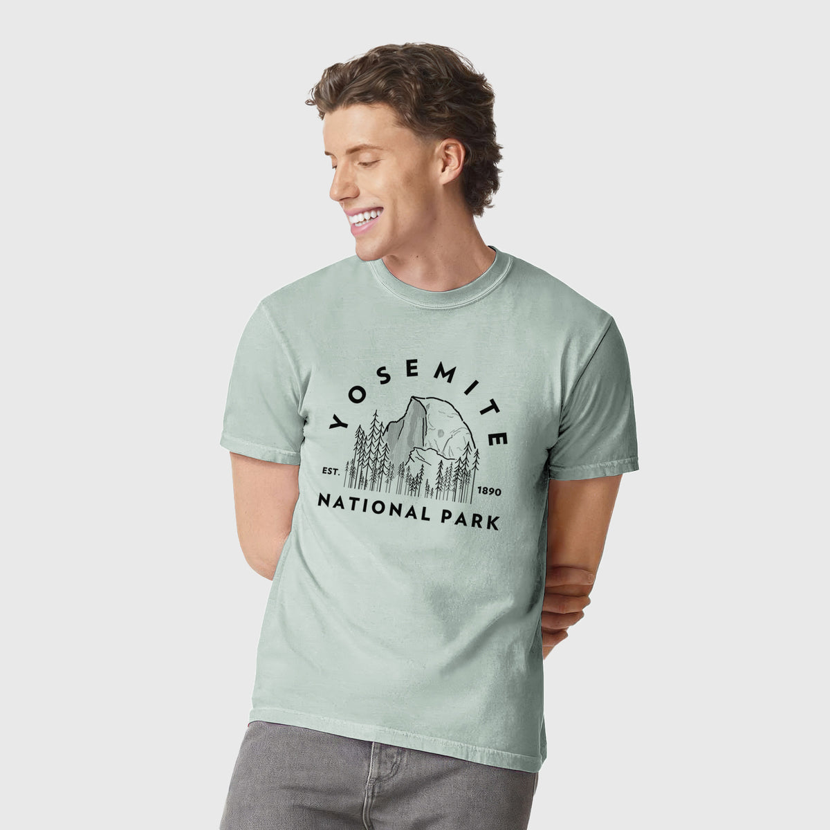 Man wearing a Comfort Colors t-shirt printed with a round badge of Half Dome and pine trees, with the words Yosemite National Park, Est. 1890.
