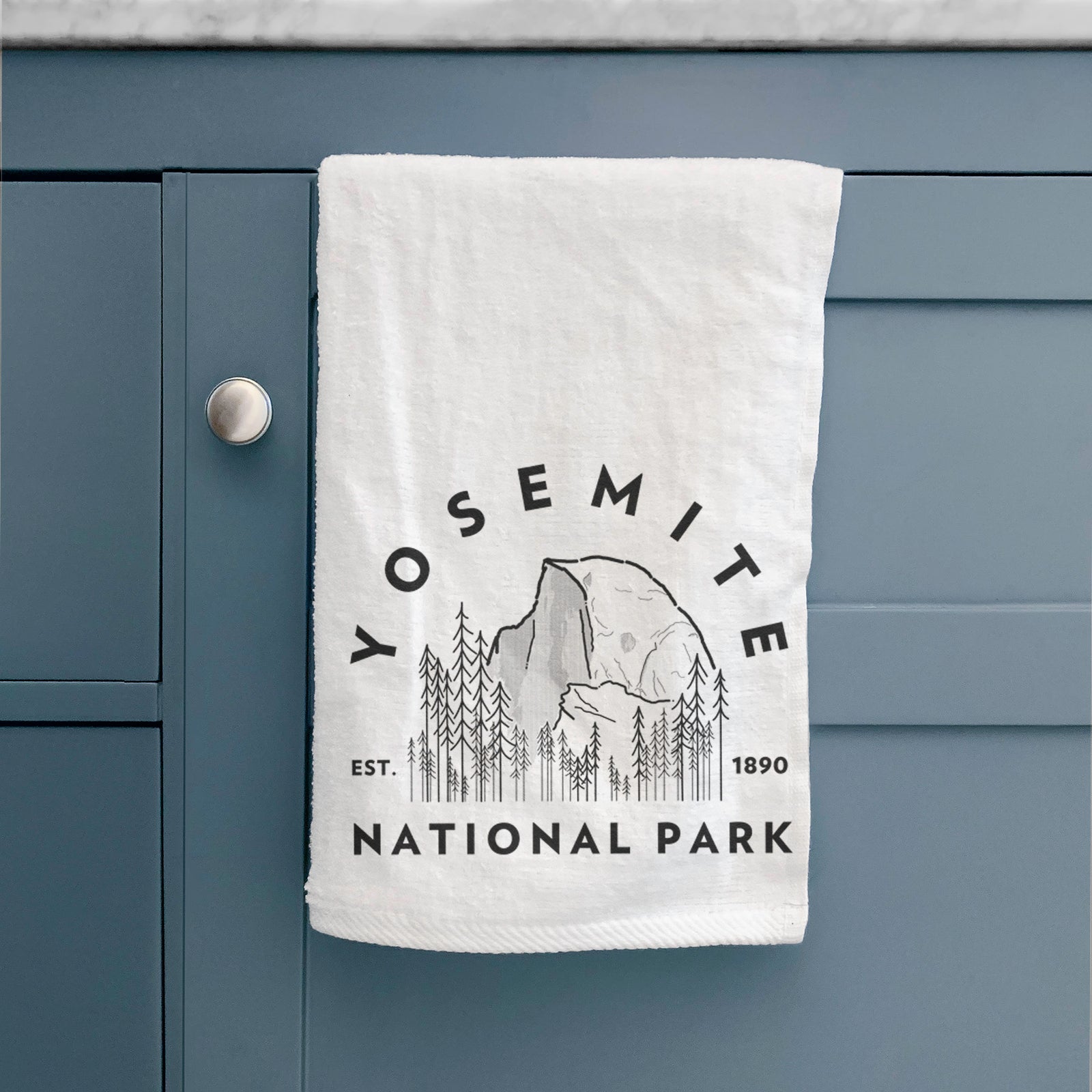 White hand towel printed with a round badge of Half Dome and pine trees, with the words Yosemite National Park, Est. 1890.