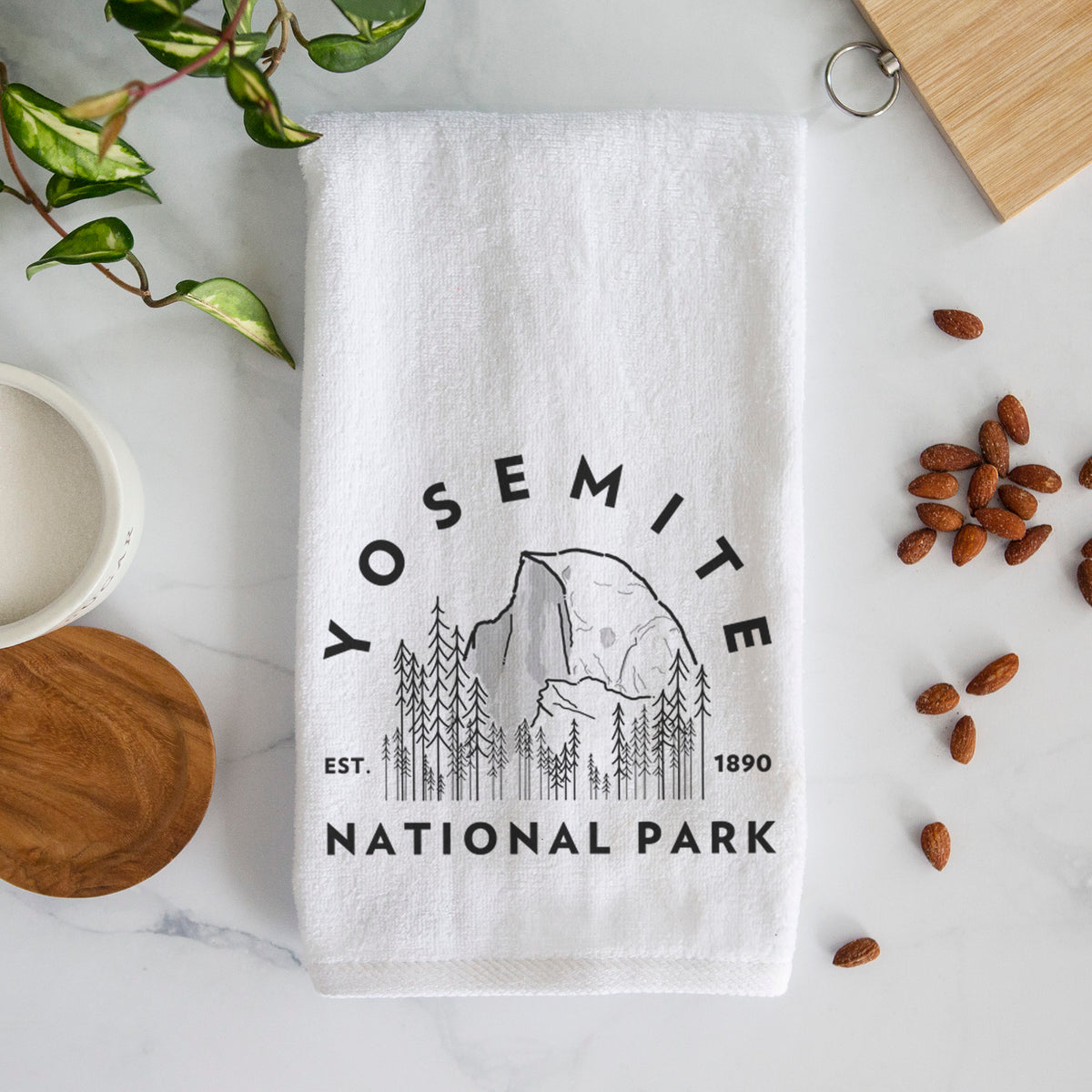 White hand towel printed with a round badge of Half Dome and pine trees, with the words Yosemite National Park, Est. 1890.