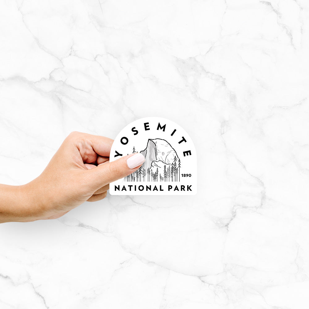 Hand holding a 4 inch vinyl decal of a round badge of Half Dome and pine trees, with the words Yosemite National Park, Est. 1890.