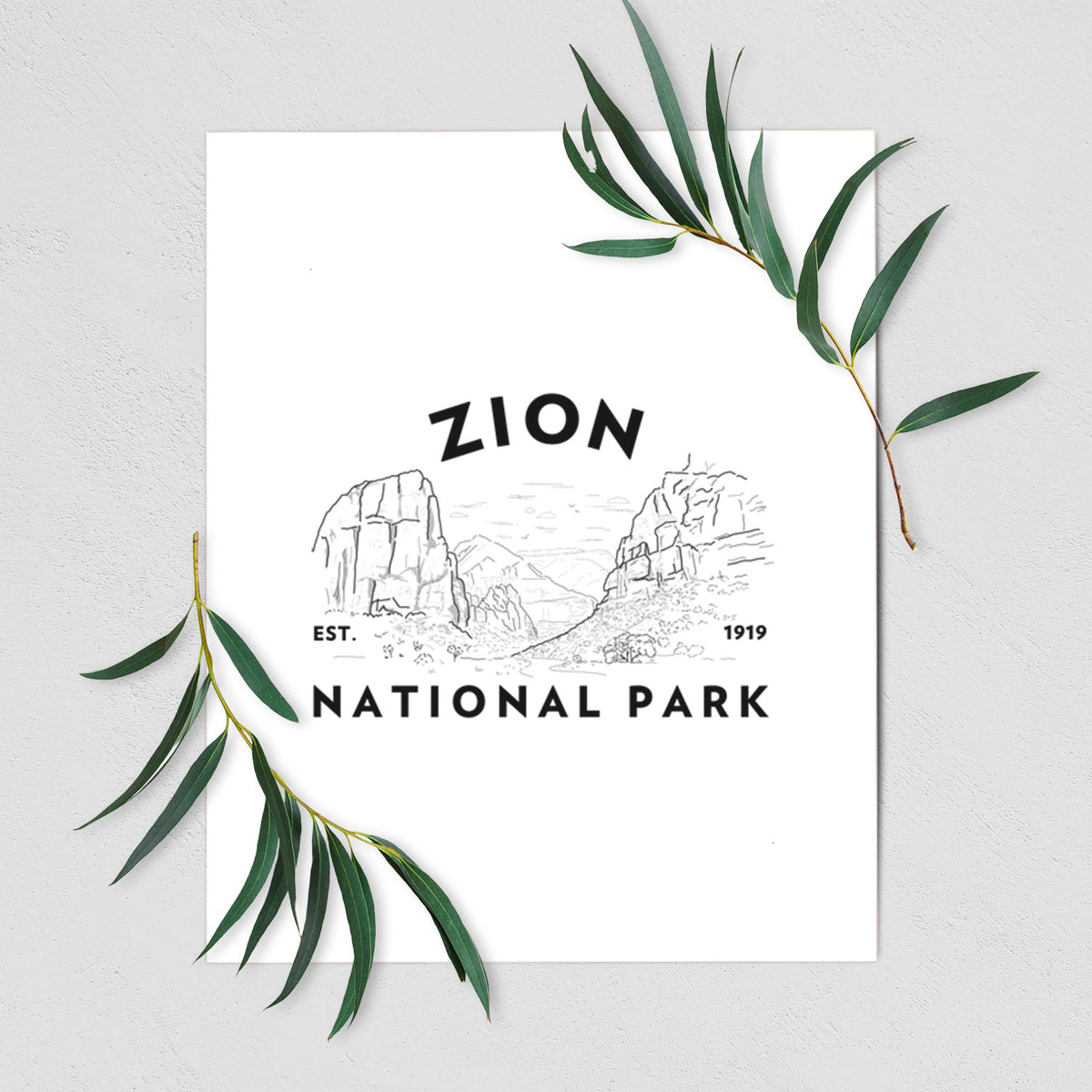 Art print of a round badge of canyon walls, with the words Zion National Park, Est. 1919, shown with eucalyptus leaves.