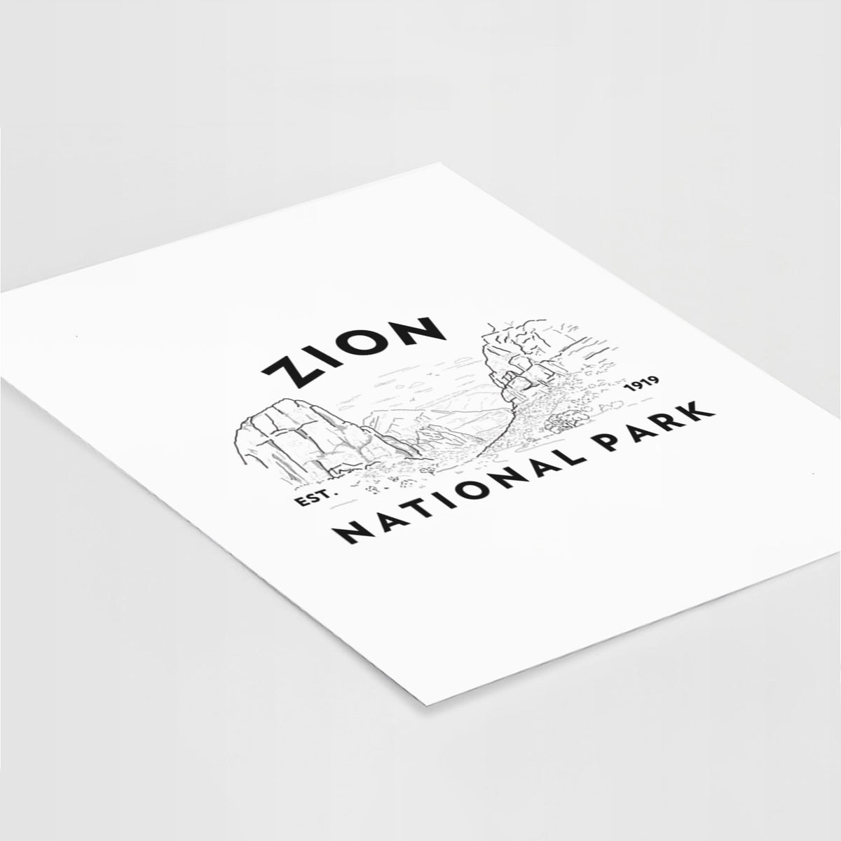 Art print of a round badge of canyon walls, with the words Zion National Park, Est. 1919, lying at an angle on a white surface.