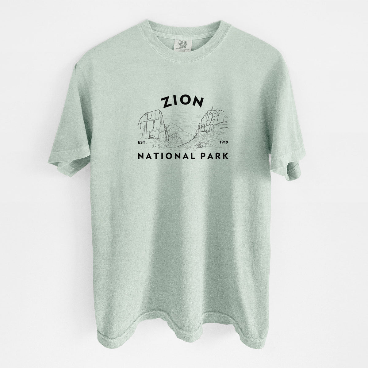Bay green Comfort Colors t-shirt laid flat, printed with a round badge of canyon walls, with the words Zion National Park, Est. 1919.