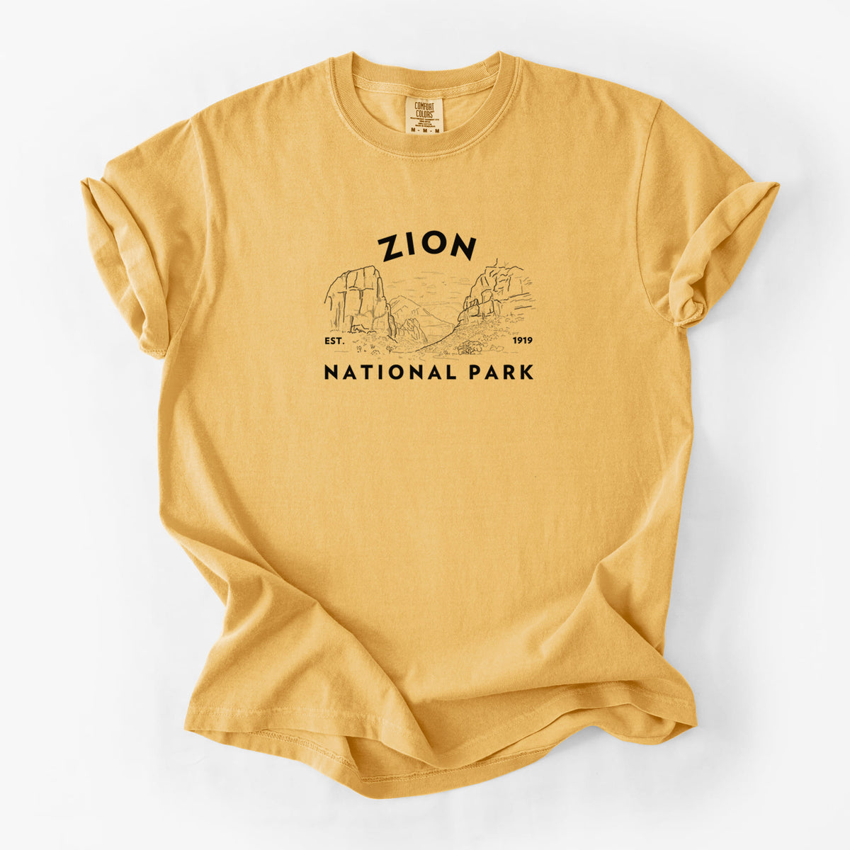 Golden wheat yellow Comfort Colors t-shirt laid flat, printed with a round badge of canyon walls, with the words Zion National Park, Est. 1919.