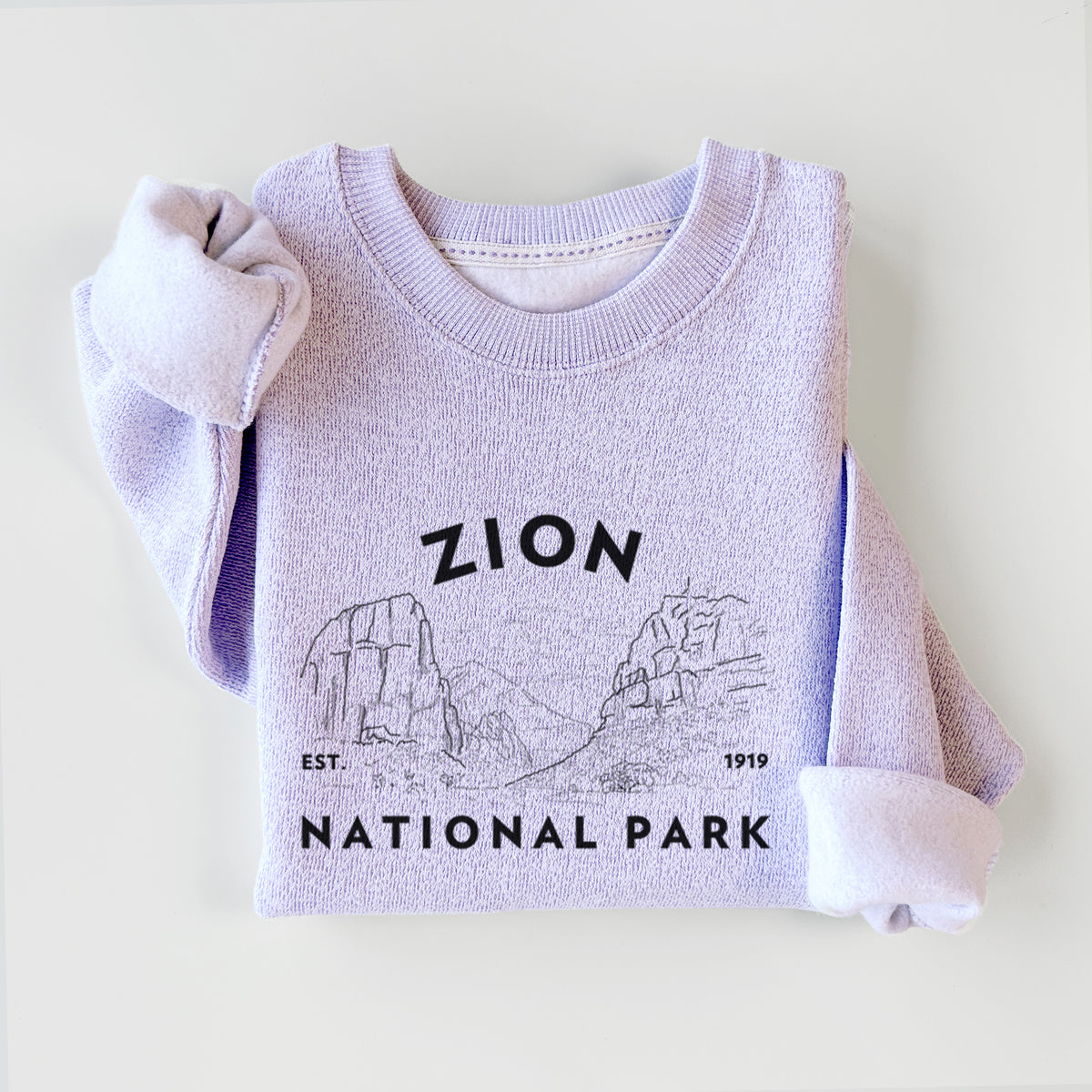 Ice purple knit sweatshirt printed with a round badge of canyon walls, with the words Zion National Park, Est. 1919, styled flat.